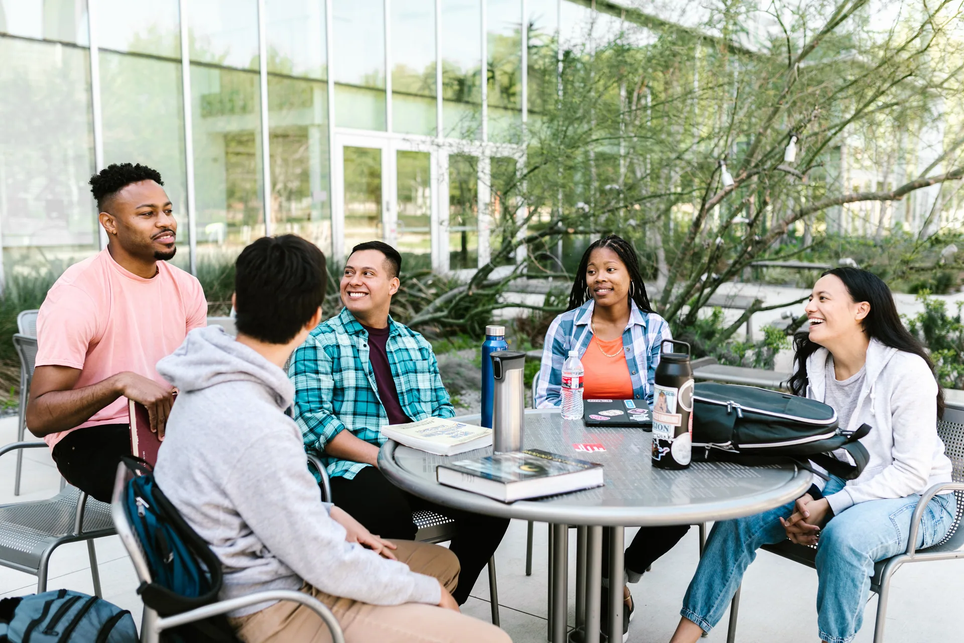 A diverse group of university students talking together around an outdoor campus table
